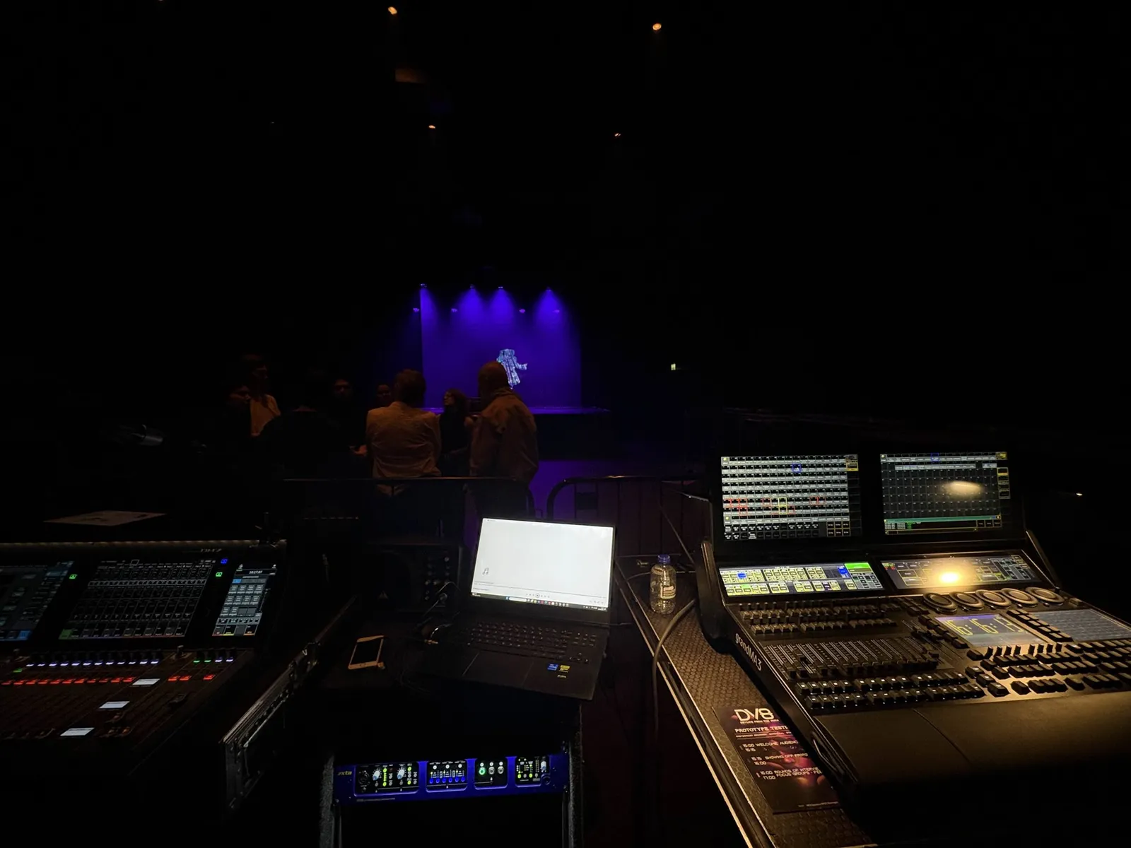 Lighting and sound desks in the dark venue, with the stage lit purple in the background
